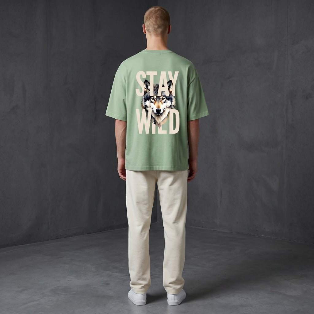 WOFF unisex sage green oversized terry tee with Stay Wild wolf graphic on the back, worn by a man in cream trousers.