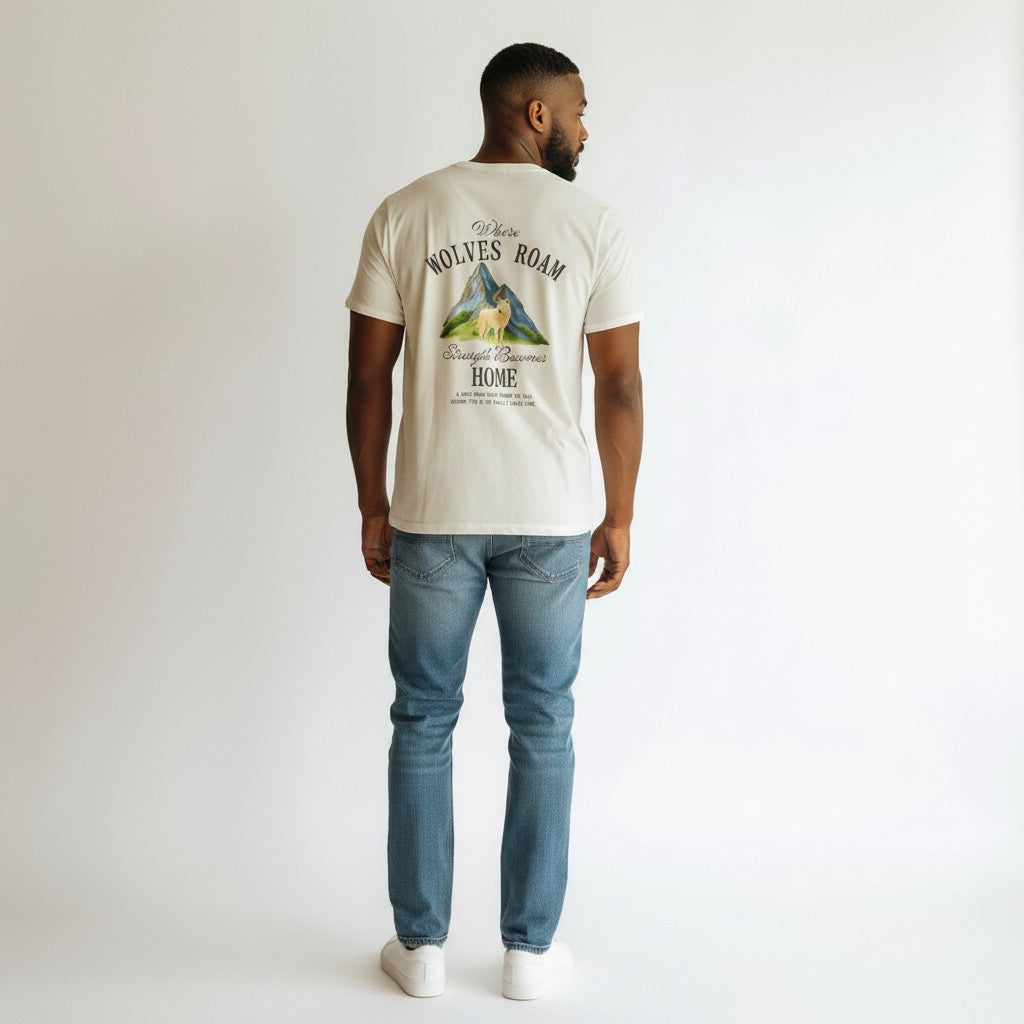 White 100% cotton WOFF t-shirt with a graphic of a wolf standing in front of mountains and text that reads "Where Wolves Roam Strength Becomes Home."